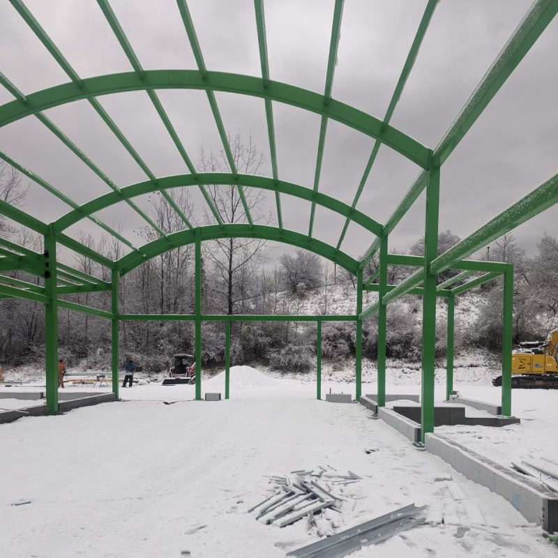 A snow-covered green metal structure with a roof, standing alone in a wintry landscape.