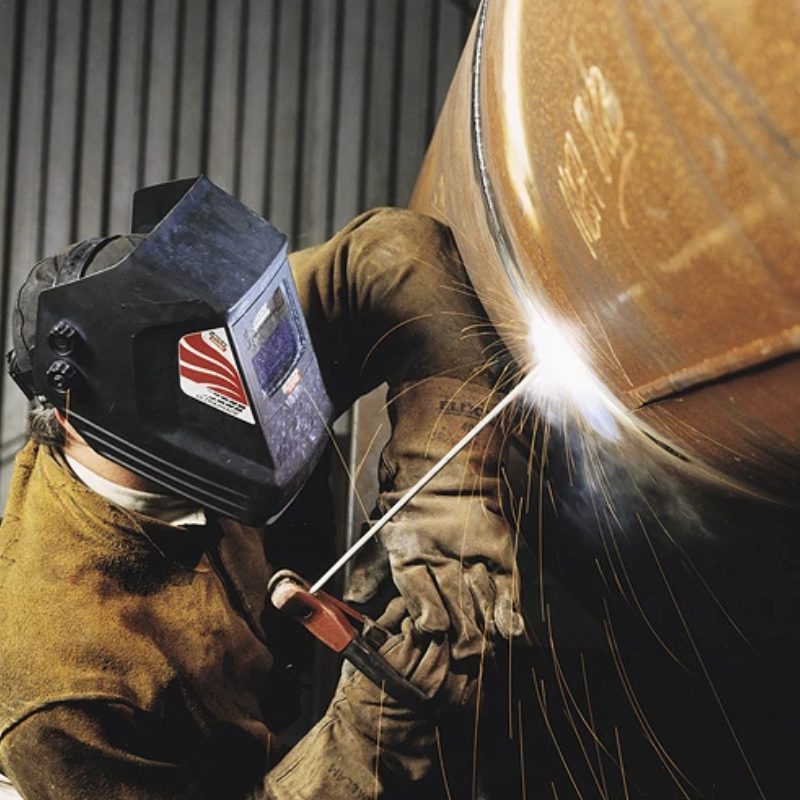 A worker welding a pipe in a factory, creating sparks as he joins the metal pieces together.
