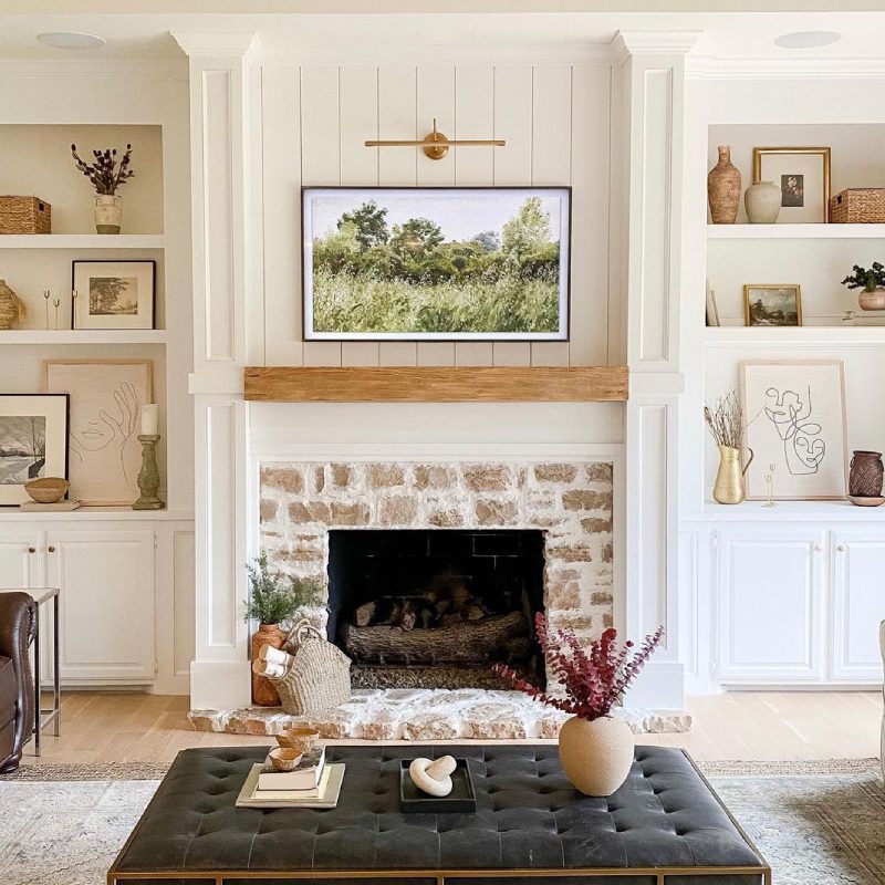 A cozy living room with a fireplace, white walls, and a large picture hanging above the fireplace.